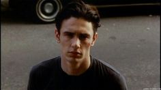 a young man standing in front of a car with his hand on his hip and looking at the camera