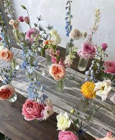 several vases filled with different colored flowers sitting on a wooden table in front of a mirror