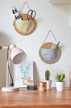 three wall hangings on the wall above a desk with various office supplies and plants