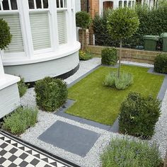 a small garden with grass and bushes in front of a white house on a checkered floor