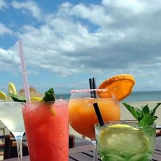 three different types of drinks sitting on top of a wooden table next to the ocean