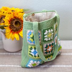 a crocheted bag sitting next to a sunflower and a mug on a table