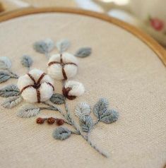 a close up of a embroidery on a wooden hoop with cotton balls and leaves in it