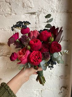 a person holding a bouquet of flowers in front of a white brick wall with greenery