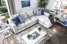 a living room with white couches and blue throw pillows on the coffee table in front of a large window