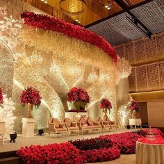 an elaborately decorated stage with red flowers and greenery in the center, surrounded by chairs