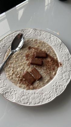 a white plate topped with oatmeal next to a spoon on top of a table