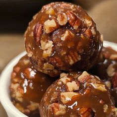 three chocolate covered donuts with nuts in a white bowl on top of a table