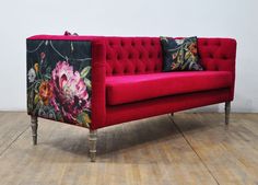 a red couch sitting on top of a hard wood floor next to a white wall