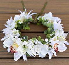 a wreath with white flowers and greenery on a wooden surface, ready to be used as a decoration