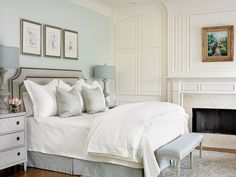 a bed with white sheets and pillows in a bedroom next to a fire place on the wall