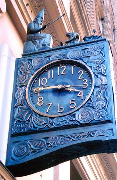 a large blue clock hanging from the side of a building with statues on it's sides