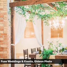 a table set up for an event with white drapes and greenery hanging from the ceiling