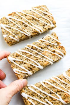 someone is holding their hand over some granola bars that are drizzled with white icing