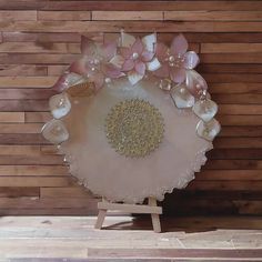 a white plate with pink flowers and pearls on it sitting on a stand against a wooden wall