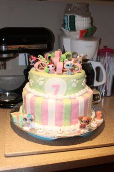 a multi layer cake decorated with littlest pet shop figures and numbers on it's side