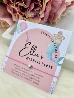 a mermaid themed party thank you card with a heart charm on it and flowers in the background