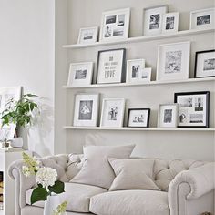 a living room filled with white furniture and pictures on the wall above it's fireplace