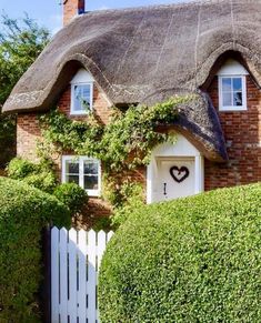 a thatched roof house with a white picket fence and heart shaped wreath on the door