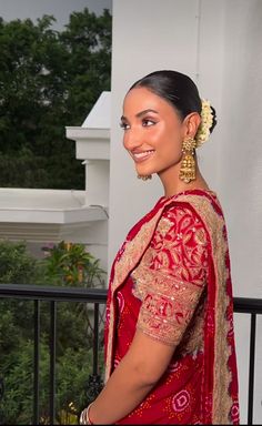 a woman in a red and gold sari smiles at the camera while standing on a balcony