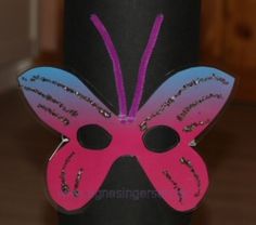 a pink and blue butterfly mask sitting on top of a black cylinder