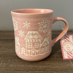 a pink coffee mug sitting on top of a wooden table next to a small tag