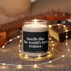 a candle that reads smells like the world's best trainer next to a guitar