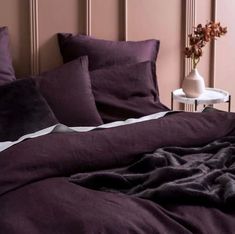 a bed with purple sheets and pillows next to a white vase on the side table