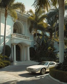 a white car parked in front of a large house with palm trees and bushes around it