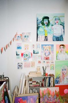 many paintings are hanging on the wall in an art room with books and other items