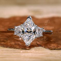 a three stone diamond ring sitting on top of a wooden table next to a leaf