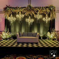 a couch sitting under a chandelier in front of a wall with flowers and greenery