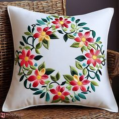 a white pillow with red and yellow flowers on it sitting on a wicker chair