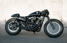 a black motorcycle parked on the side of a road next to a building with white walls