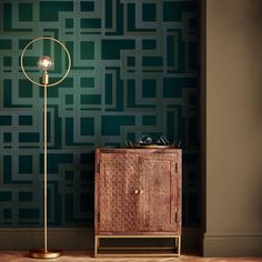 a floor lamp next to a wooden cabinet in front of a wall with green squares on it