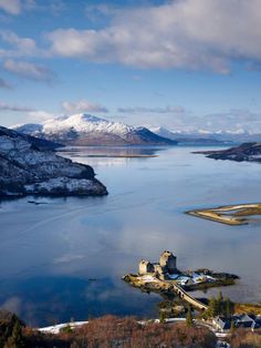 an aerial view of a castle in the middle of water with mountains in the background