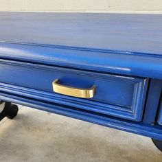 a blue table with two drawers and a gold handle on it's top, sitting in a room