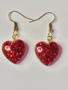 These beautiful red sparkling heart dangle gold color earrings are the perfect way to show off your unique style. This eye-catching accessory are handmade and is sure to turn heads and also draw compliments. The brilliant red sparkling glitter adds a touch of elegance and drama to any outfit. They are also a great way to add a little bit of sparkle and shine to any ensemble. Not only that, but these earrings make a great gift for her,  a friend or loved one, as they will be sure to make them fee Affordable Round Earrings For Valentine's Day, Heart Print Dangle Jewelry For Gifts, Trendy Red Heart Earrings For Gift, Trendy Heart Print Earrings For Gift, Glitter Jewelry Gift, Glitter Jewelry For Gifts, Heart Shaped Earrings With Heart Print As Gift, Cute Glitter Jewelry Gift, Heart Print Earrings As Valentine's Day Gift