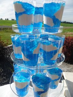 cupcakes with blue icing and white frosting are stacked on a clear cake plate