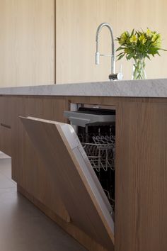 an open dishwasher in a kitchen with flowers on the counter top and wooden cabinets