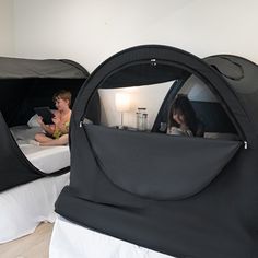 two people sitting in black tents on top of a bed