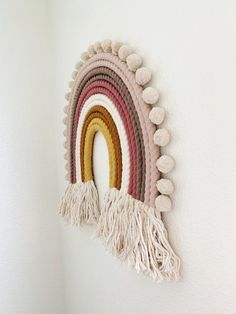 a wall hanging with a rainbow made out of yarn and pom poms on it