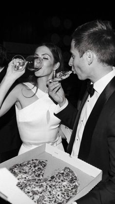 a man and woman are eating pizza and drinking wine at a formal event in black and white