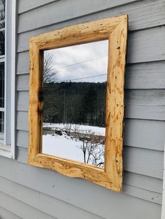 a mirror hanging on the side of a house next to a snow covered yard and trees