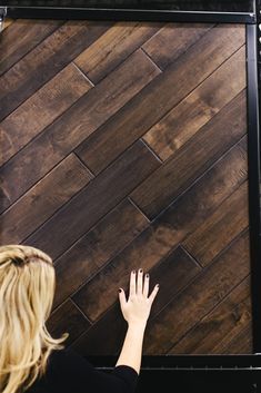 a woman standing in front of a wooden wall with her hands on the wood floor