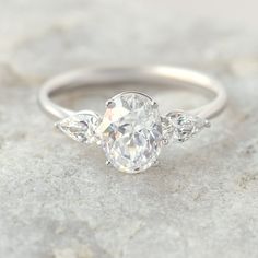 a three stone diamond ring sitting on top of a white rock with two diamonds in the middle