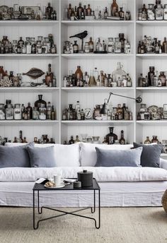 a living room with shelves filled with bottles and jars on it's wall, along with a white couch