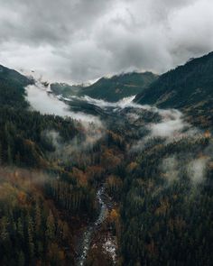 the mountains are covered in fog and low lying clouds as they rise over a river