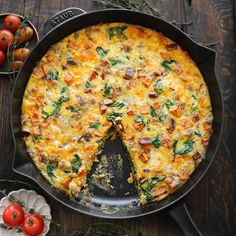 a pizza sitting in a pan on top of a table next to tomatoes and herbs