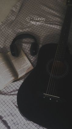 an acoustic guitar and book on a bed